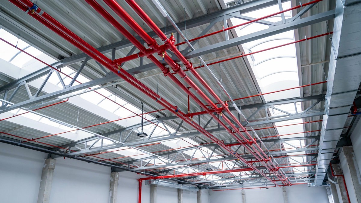 Red de tubería roja de rociadores contra incendio instalada bajo la cubierta de una nave industrial